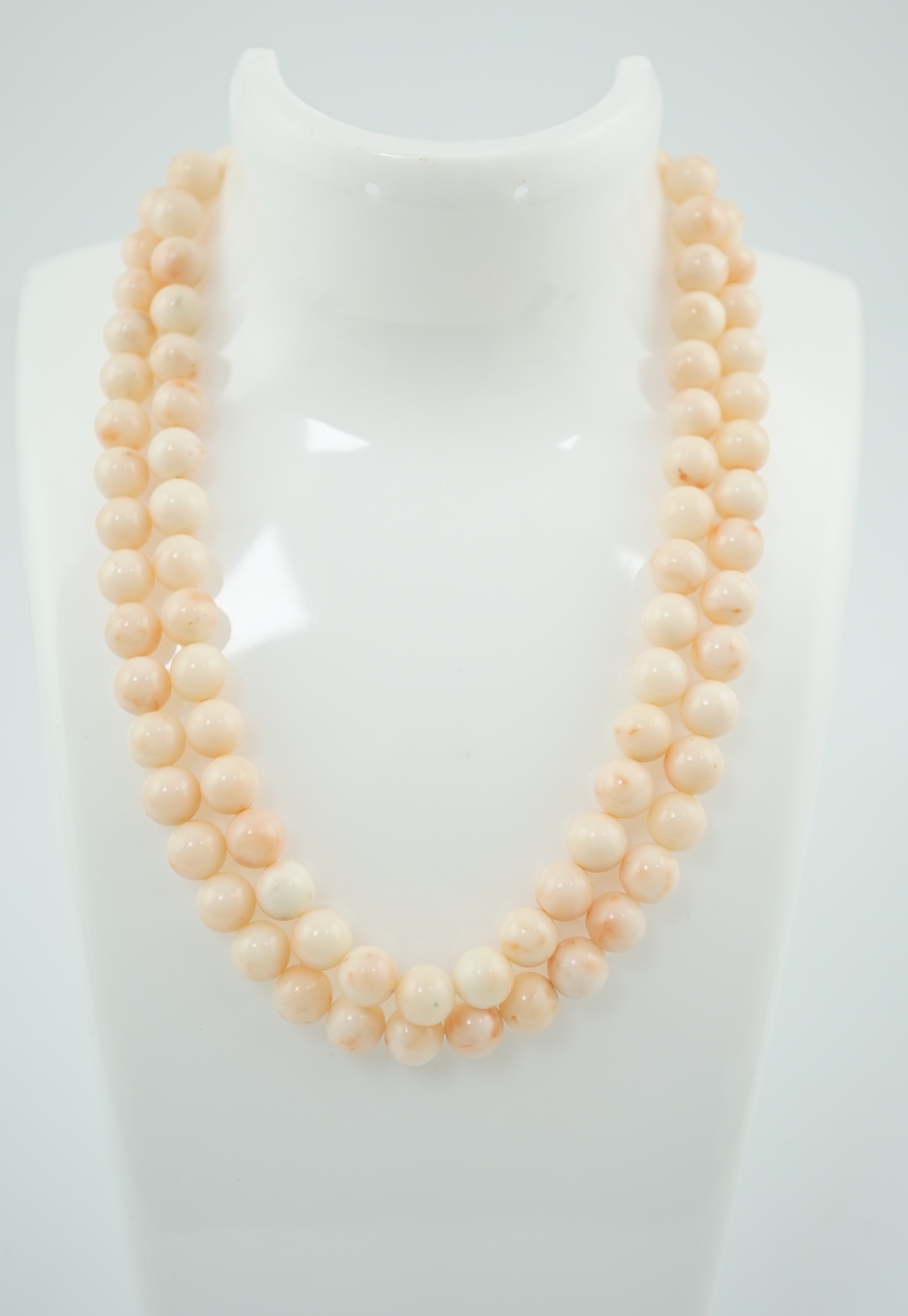 A double strand pale pink coral bead choker necklace, with round and baguette cut diamond cluster set bow shaped 18k white gold clasp